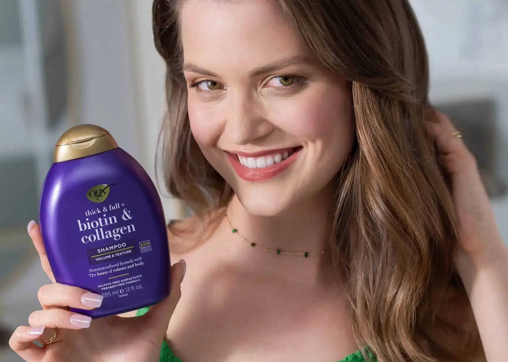 Image displaying woman with healthy hair holding OGX Biotin and Collagen Shampoo 13oz